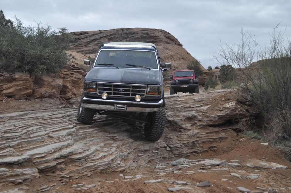 Dark gray Ford Bronco with a roof rack navigates a rocky off-road trail