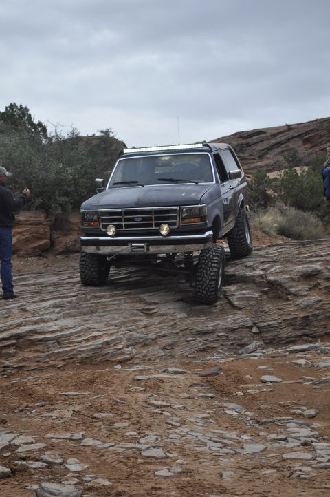 1991 Ford Bronco - A Ford Bronco navigates a rocky off-road trail under a cloudy sky.