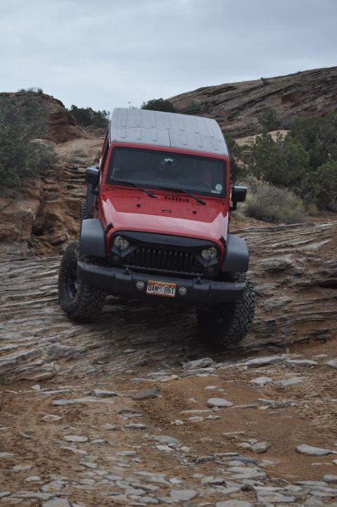 1991 Ford Bronco - A red Jeep Wrangler navigates a challenging rocky terrain under an overcast sky.