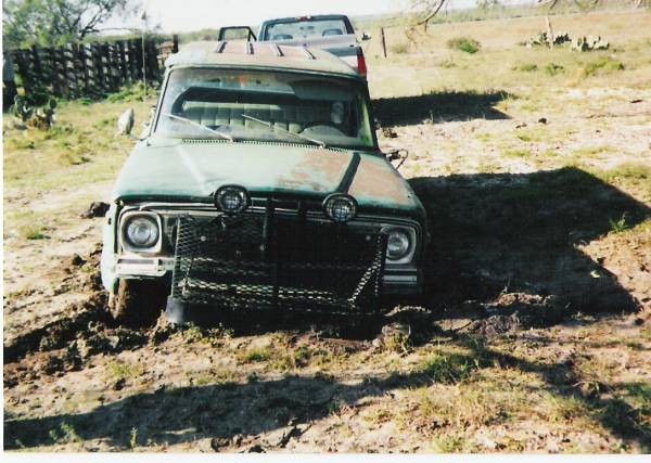 Faded green Jeep SJ wagon with mesh grille guard stuck bumper-deep in pasture mud