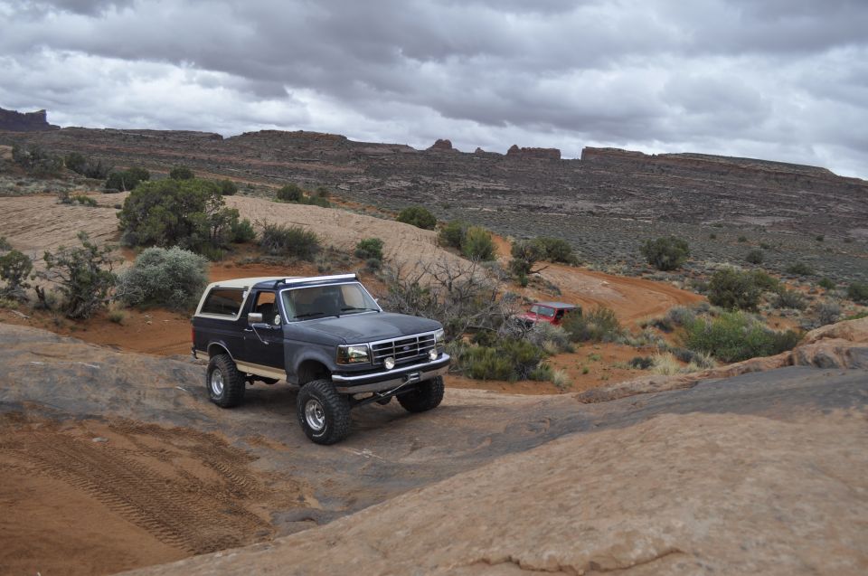 Dark blue Ford Bronco with a tan top and off-road tires on a rocky trail