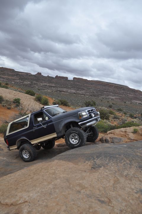 1991 Ford Bronco - This SUV navigates a rocky trail under a cloudy sky.
