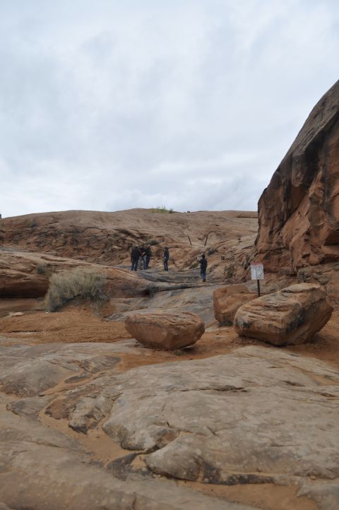 1991 Ford Bronco - A group of people stand in a desert landscape with large rock formations and sparse vegetation under a cloudy sky.