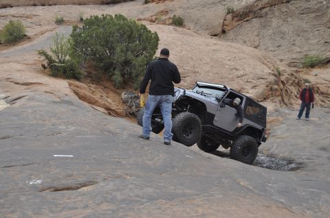 1991 Ford Bronco - A silver Jeep Wrangler navigates a rocky incline with two people observing the off-road activity.