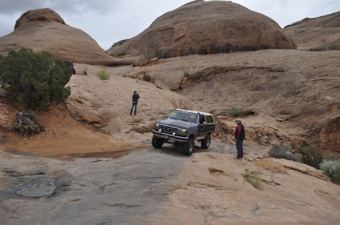1991 Ford Bronco - A Ford Bronco navigates a challenging off-road course in a desert landscape under a cloudy sky.