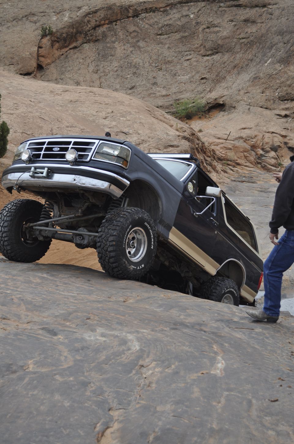 Black 1991 Ford Bronco climbing rocky terrain with a person standing nearby