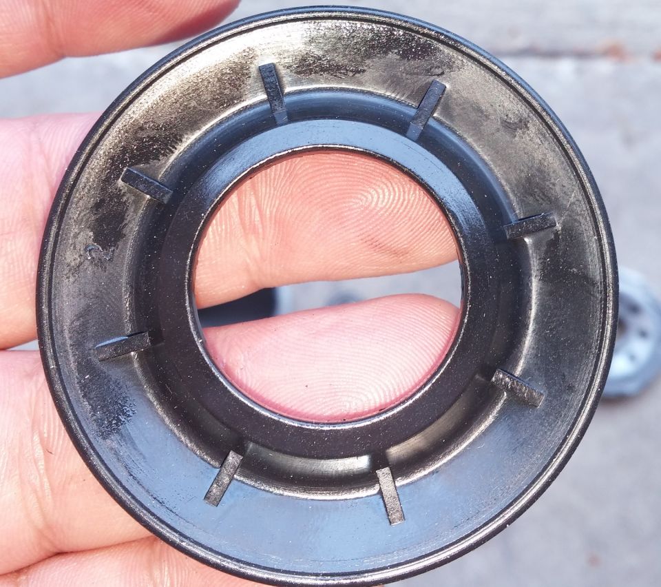 Close-up of a black plastic oil filter housing with internal tabs, held by fingers