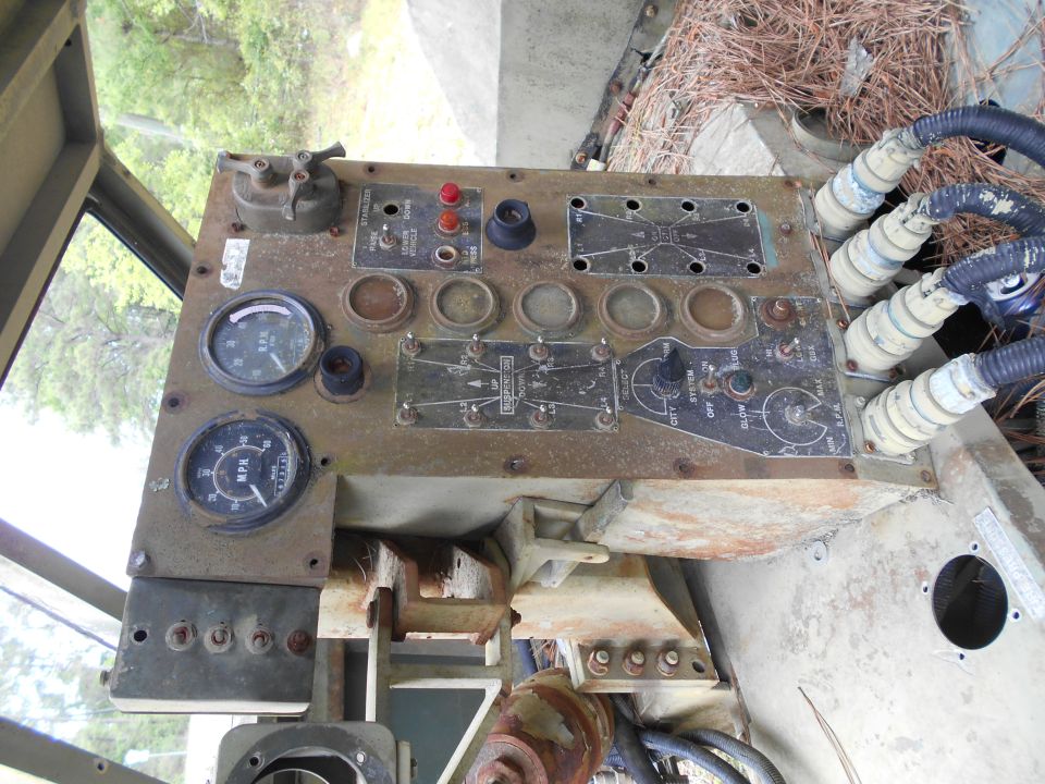 Close-up of a rusty vehicle dashboard with two gauges, multiple switches, and electrical connectors