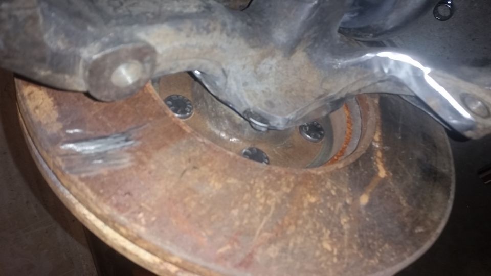 Rusty brake rotor with visible bolt heads and a metal suspension component above