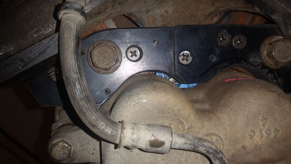 Brake caliper and bracket assembly with visible text on hose and casting
