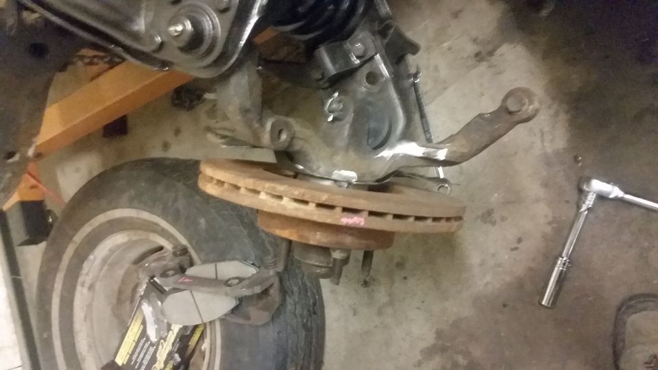 Close-up of a vehicle's front suspension assembly, showing a brake rotor and caliper bracket