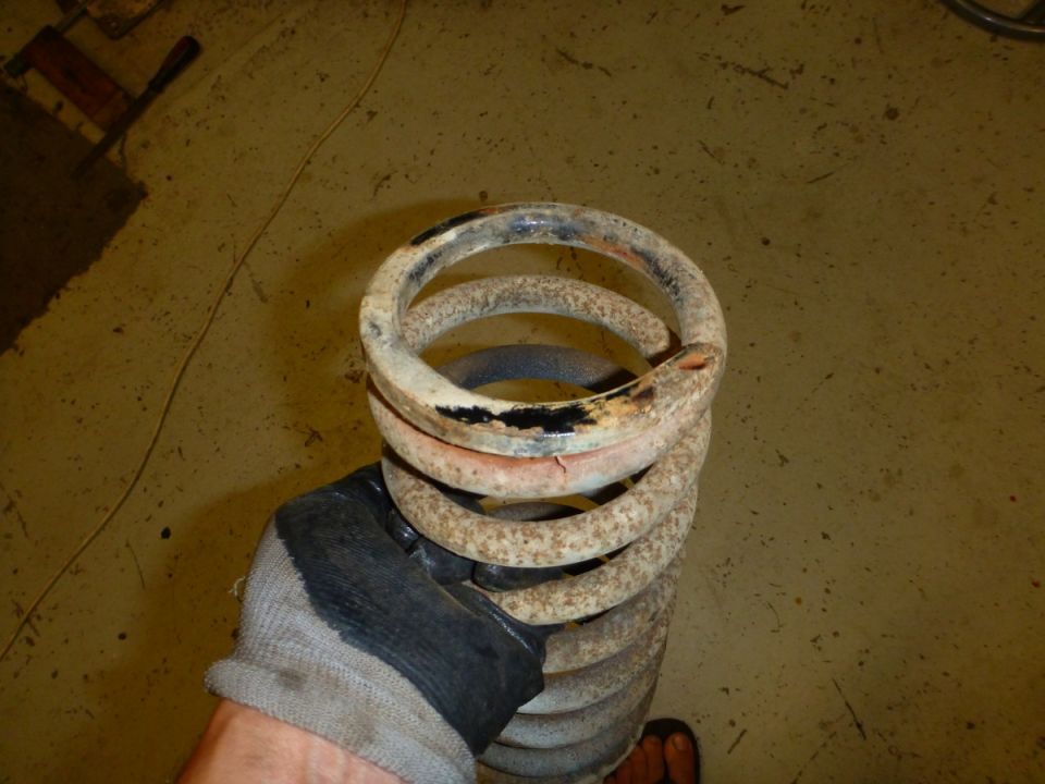 Rusty suspension coil spring held by a gloved hand