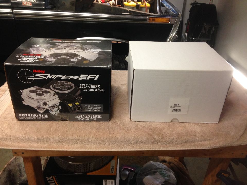 Holley Sniper EFI box next to a white box on a table. A car engine bay is visible in the background