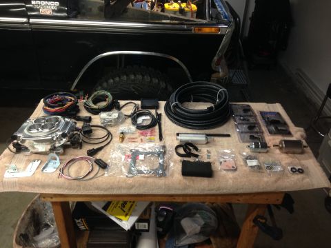 1979 Ford Bronco - Holley Sniper EFI installation parts are laid out on a table in front of a black Ford Bronco.