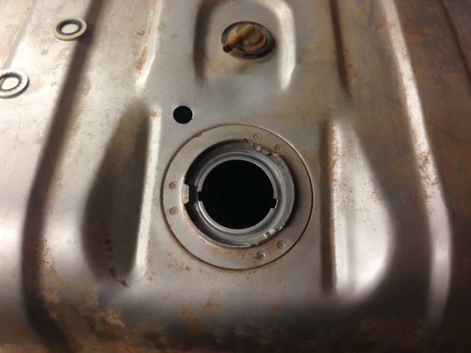 Close-up of a rusty fuel tank filler neck with a black opening