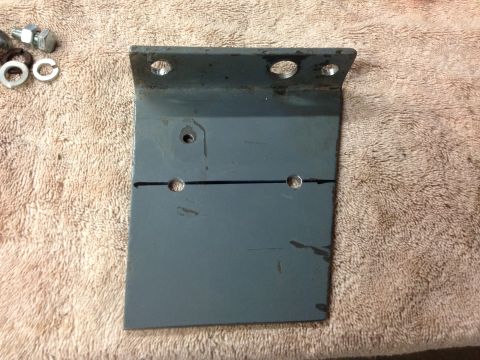 1979 Ford Bronco - A metal bracket, along with bolts and washers, is laid out on a textured cloth surface, likely for installation or repair.