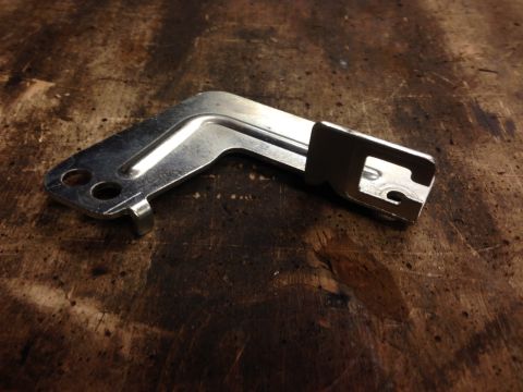1979 Ford Bronco - A metal bracket with a bent shape and two mounting holes sits on a textured wooden surface.