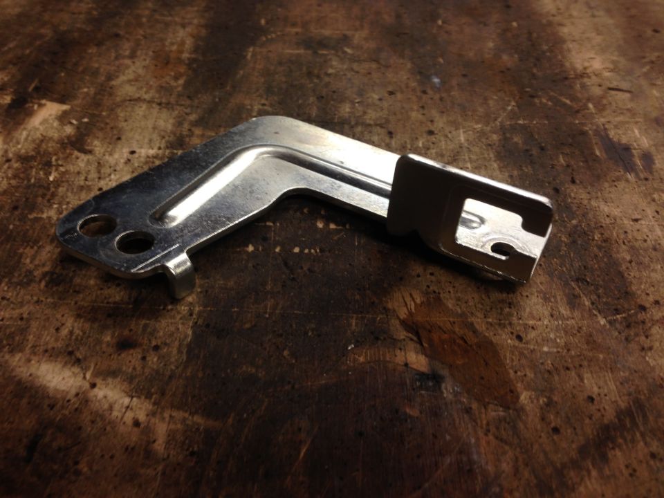 metal bracket with two holes and a tab, on a wooden surface