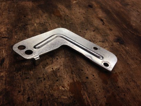 1979 Ford Bronco - A metal bracket with a bent tube and mounting holes rests on a wooden surface.