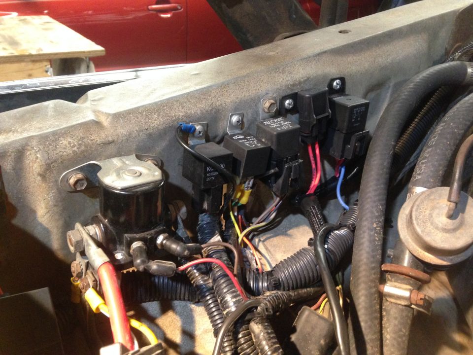 Engine bay with multiple relays and wiring harnesses. Red car interior visible in background