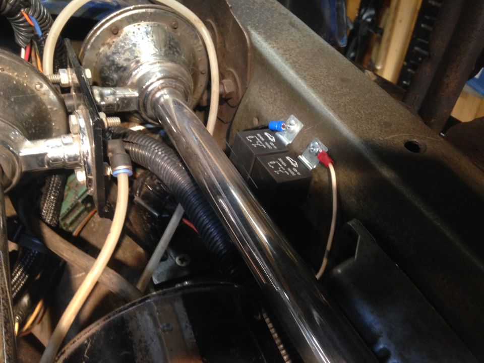 Chrome horn assembly and two black relays with wiring, mounted in engine bay