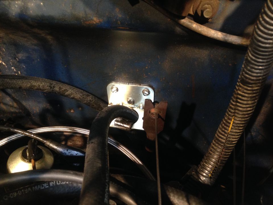 Metal bracket with screws attached to blue painted surface, near hoses and wiring