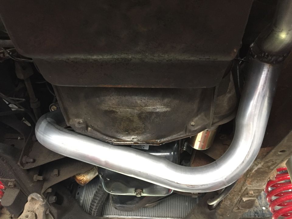 Underneath view of a vehicle's transmission housing and a shiny new exhaust pipe. Red coil springs are visible