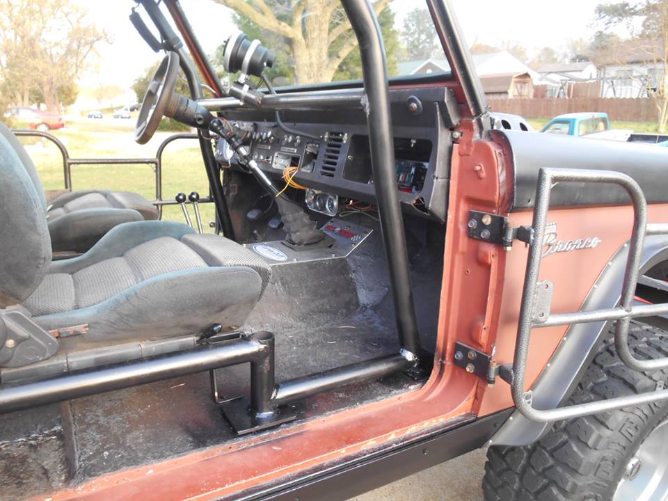 Interior of a modified Ford Bronco with roll cage, bucket seats, and custom door panel