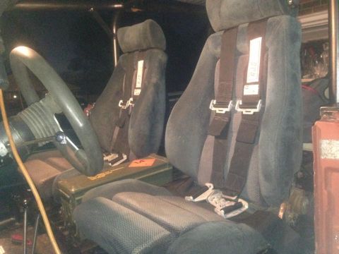 1972 Ford Bronco - The interior of a vehicle shows dark seats with racing harnesses and a green ammo box on the floor.
