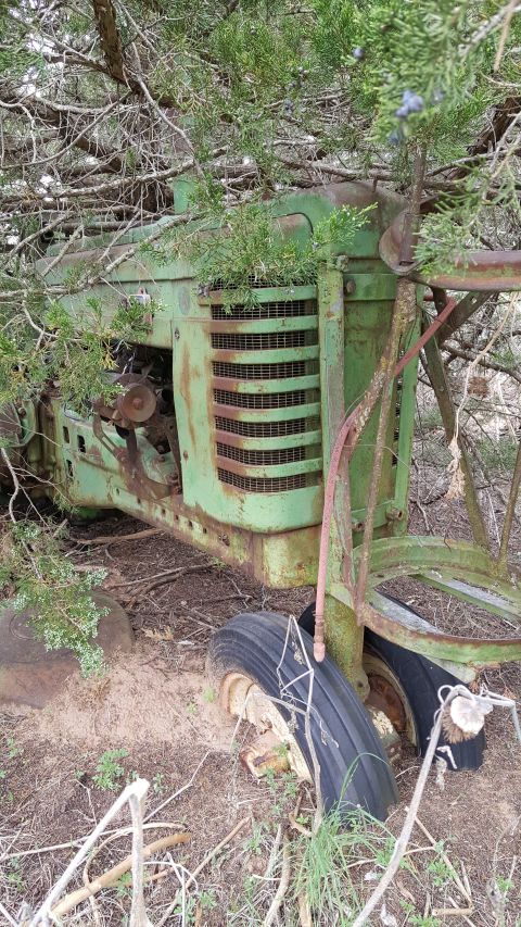 1973 Ford F-100 - An old green tractor sits abandoned and overgrown with vegetation in a wooded area.