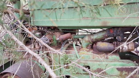 1973 Ford F-100 - Close-up view of a green tractor's engine compartment, partially obscured by tree branches and foliage.