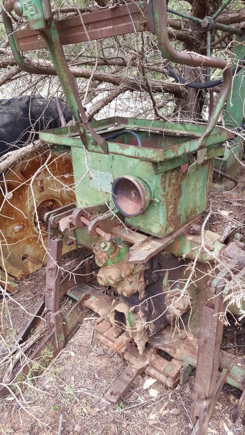 1973 Ford F-100 - A rusty green tractor attachment sits amidst dry brush and branches, with a portion of a large tire visible.