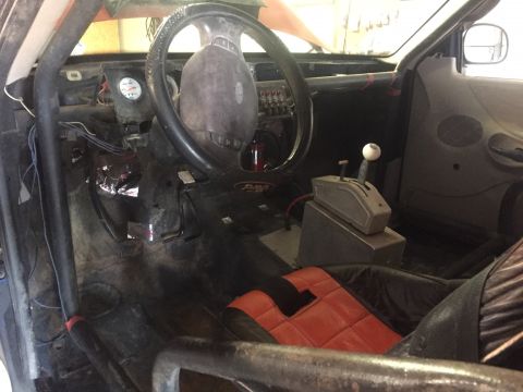 1982 Ford Bronco - The interior of a heavily modified truck shows a roll cage, racing seat, and a floor-mounted shifter with a white knob.