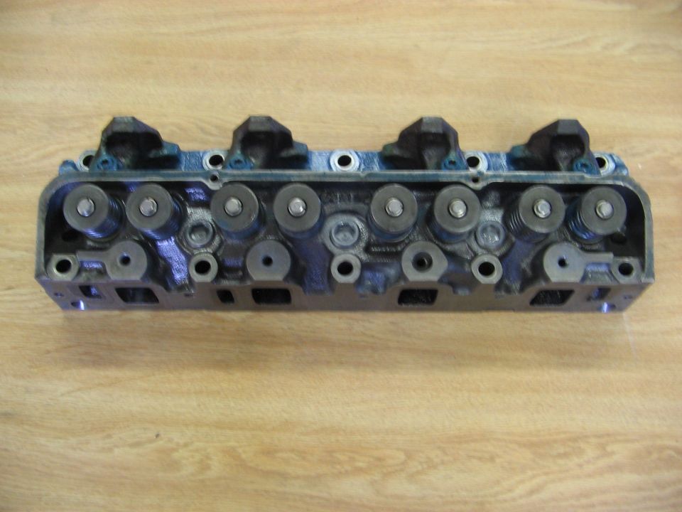 Engine cylinder head with visible valves and springs on a wooden surface