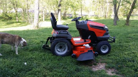 2007 Subaru Impreza - A dog sniffs around a red and black riding lawn mower in a grassy yard.