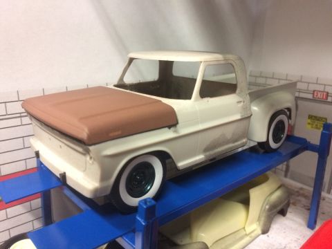 1989 Ford Bronco - Model truck with a brown hood sits on a blue lift in a garage setting.
