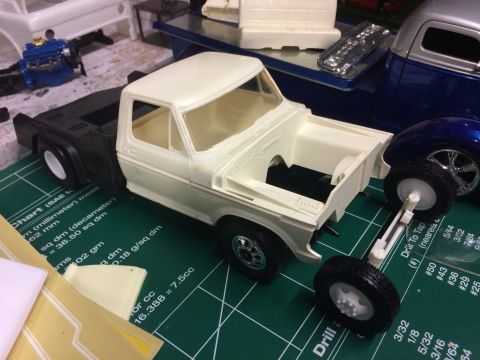 1989 Ford Bronco - A partially assembled model truck sits on a cutting mat next to other model parts and a finished blue model truck.