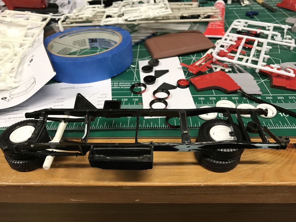 Model car chassis with wheels, tires, and various plastic parts scattered around on a cutting mat
