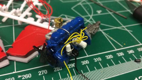 1989 Ford Bronco - A model engine, painted blue with yellow wiring, sits on a cutting mat next to model kit parts.