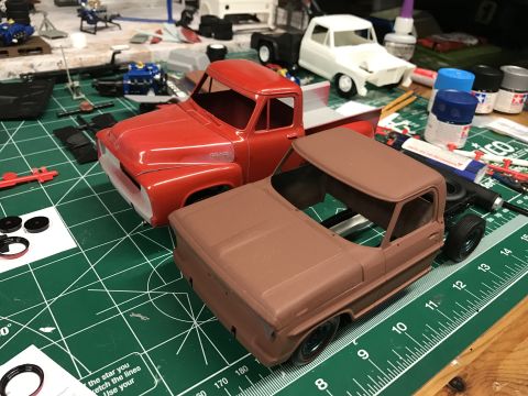 1989 Ford Bronco - Two model trucks, a red 1956 Ford F-100 and a brown one, sit on a green cutting mat surrounded by model building supplies.