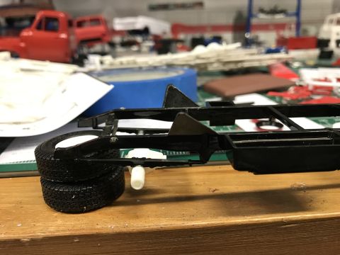 1989 Ford Bronco - A model truck chassis with wheels is shown on a wooden surface, with other model parts in the background.