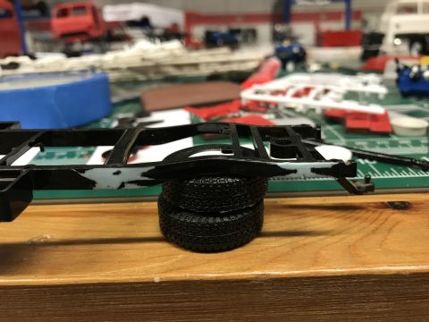 1989 Ford Bronco - A model car chassis and tires are shown on a workbench, surrounded by various crafting supplies and other model parts.