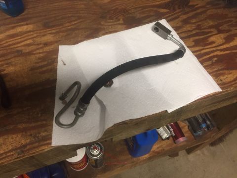 1982 Ford Bronco - A power steering hose lies on a paper towel on a wooden surface.