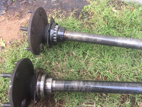 1982 Ford Bronco - Close-up of two vehicle axle shafts with their associated hubs and bearings resting on a grassy surface.