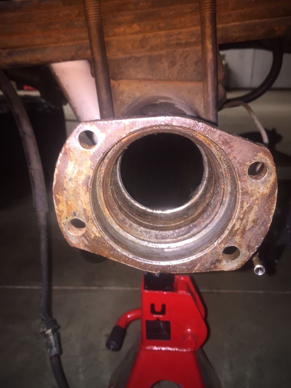 Close-up of a rusted axle housing flange with four bolt holes, supported by a red jack stand