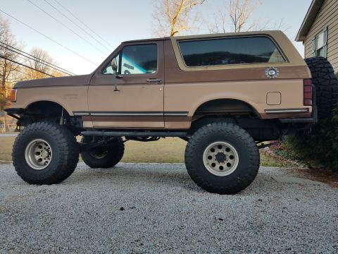 1988 Ford Bronco - This lifted 1988 Ford Bronco features a two-tone brown paint scheme and is equipped with large off-road tires.