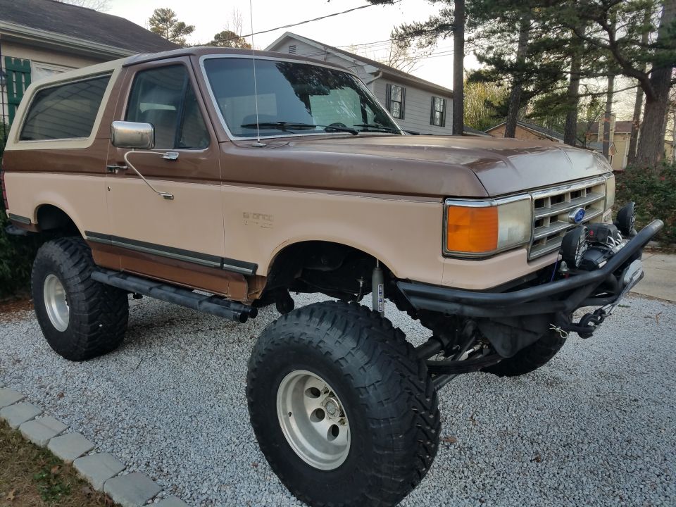 Brown and tan Ford Bronco with lifted suspension and large tires, front-left view
