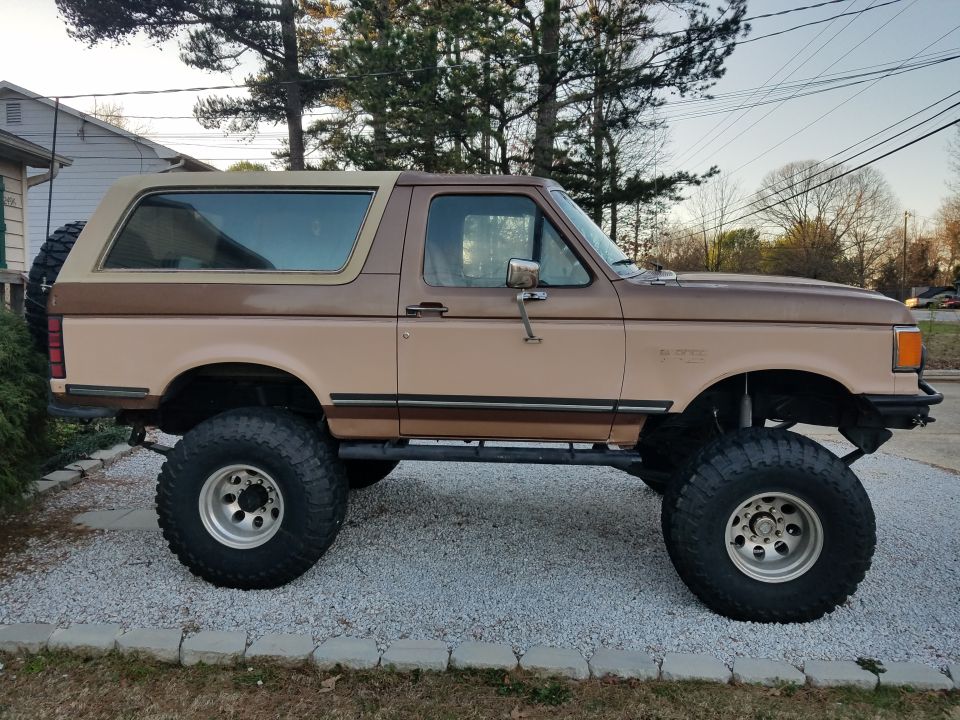 Side view of lifted two-tone brown SUV with large tires and spare tire on rear