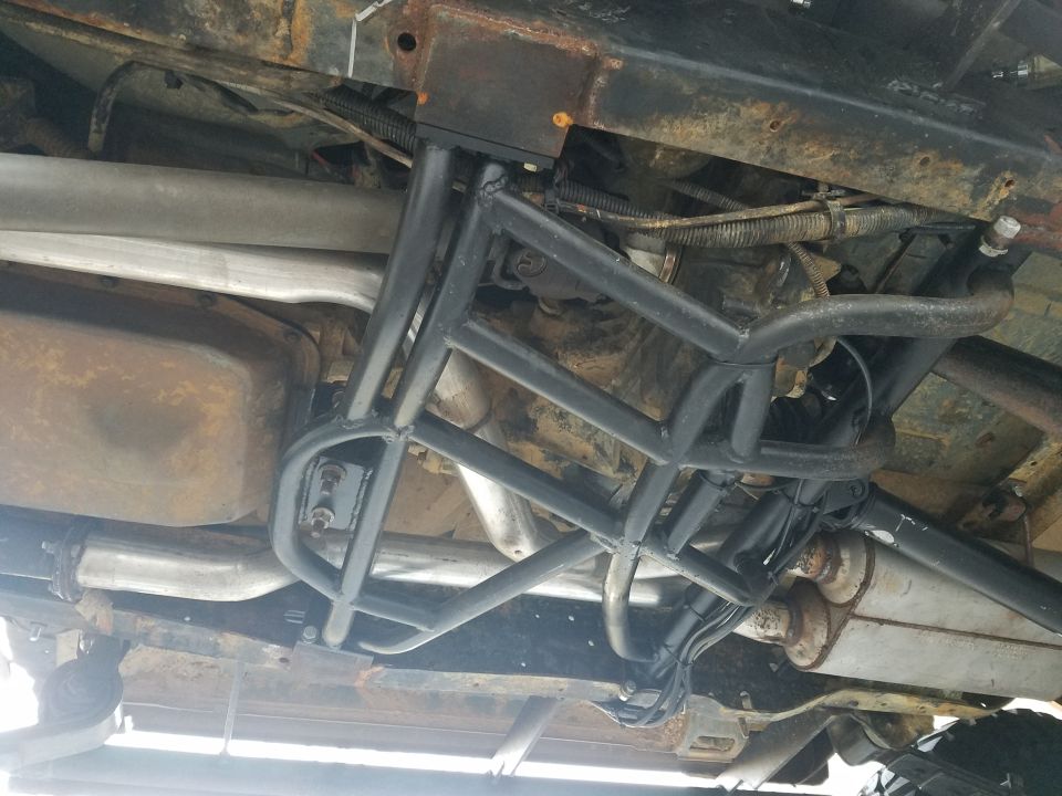Underbody view of a vehicle showing a custom roll cage, exhaust system, and transmission components