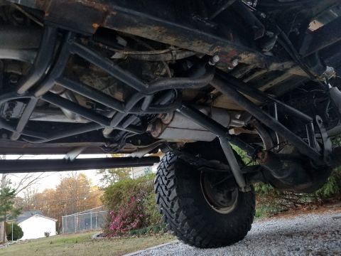 1988 Ford Bronco - The underside of a heavily modified SUV shows a complex roll cage and large off-road tires.